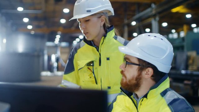 Male Industrial Engineer Works on the Personal Computer while Female Manager Talks about Project Details. They Work in Heavy Industry Manufacturing Factory.