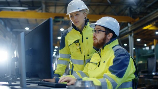 Male Industrial Engineer Works on the Personal Computer while Female Manager Talks about Project. They Work in Heavy Industry Manufacturing Factory.