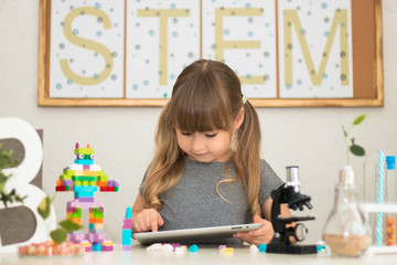 Little girl is behind the desk. Microscope, the tree, little robot and books are near her. The word STEM is on the background. E-learning. Stem education. Cute child.
