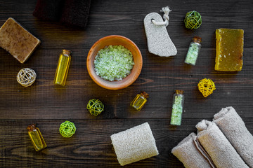 Foot spa cosmetics. Spa salt, oil, pumice stone, soap and towel on dark wooden background top view