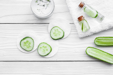 Lotion with cucumber on white wooden background top view