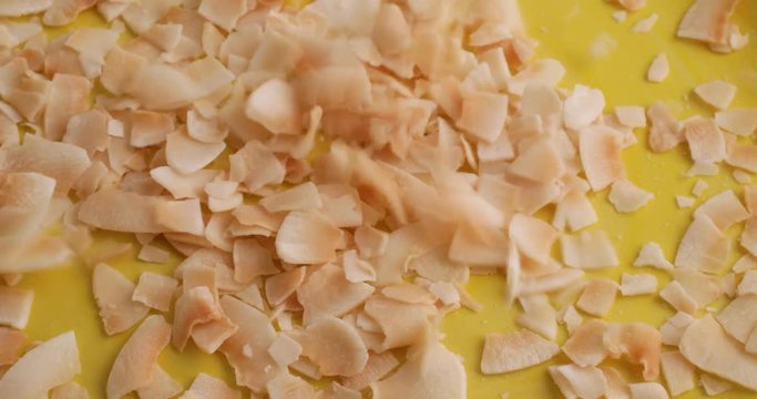 Close video of pouring freshly toasted coconut flakes into a bright yellow dish.