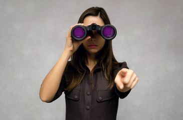 Young caucasian woman looking through binoculars with glamour purple lens and showing ahead by her index finger. Find and search. Find something interesting.