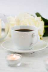Coffee for breakfast or lunch with decorations, candles and flowers. white roses on the table and cup of coffee