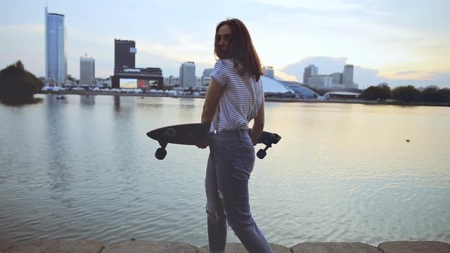 Young girl holding a skateboard and whirl around her on the city waterfront