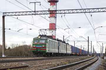 Fototapeta na wymiar The locomotive of a freight train drags the composition of containers on platforms of a railway track.