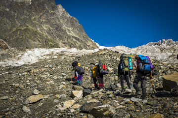 Tourists in the Caucasian Mountains. A group of tourists goes to a mountain pass on a stony slope and glacier.