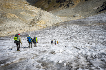Tourists in the Caucasian Mountains. A group of tourists descends from the mountain pass on the remnants of the glacier.