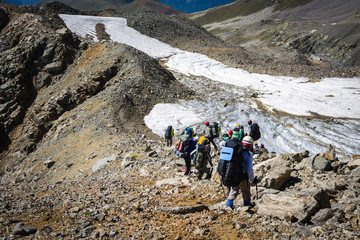 Tourists in the Caucasian Mountains. A group of hiking tourists descends from a mountain pass along a steep stony slope. The weather facilitates complex movement in the highland area.