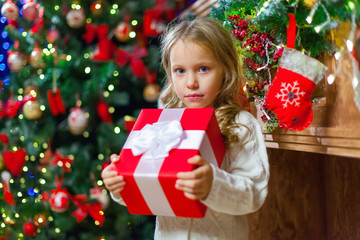 Little girl sitting by the tree holding a Christmas gift