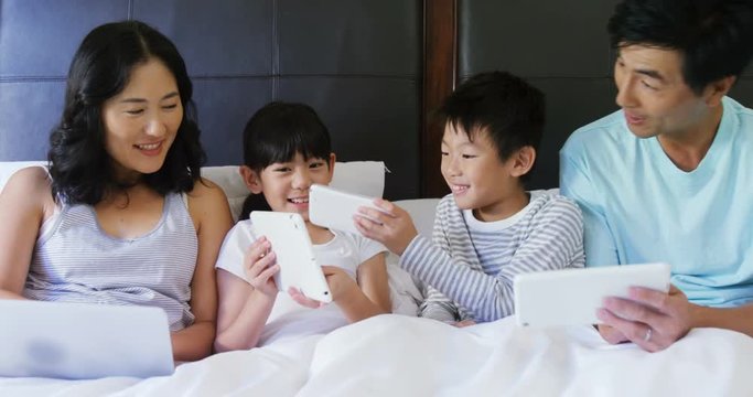 Happy family using electronic devices in bedroom 