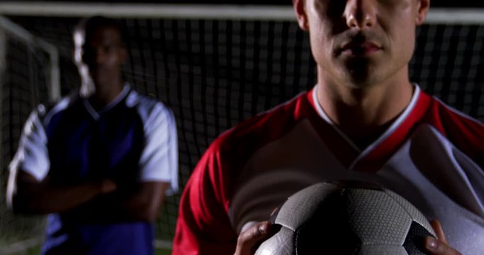 Portrait of confident soccer player holding ball with rival athlete 