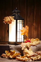 Vertical front view of an old Asian design lantern and white candle glowing brightly inside with autumn decorations on rustic wood.