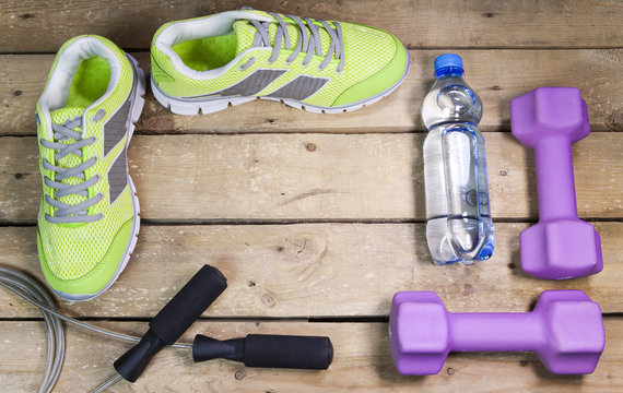Sports sneakers, dumbbells, drinking water on a wooden background,  flat lay