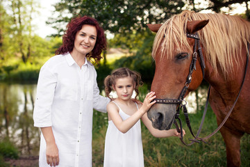 Mother and daughter are petting a horse. Summer meadow.