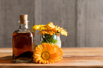 A bottle of calendula tincture with calendula flowers on a wooden background