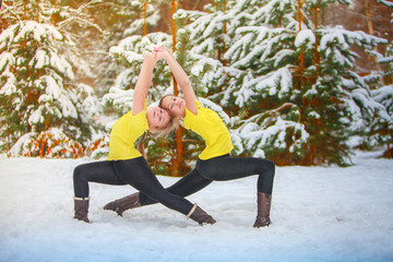 two beautiful women  doing yoga outdoors in the snow