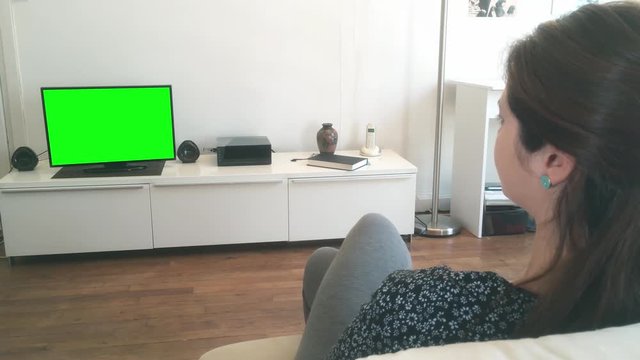 Young Woman At Home Watching Green Screen Television. Charming young woman watching green screen television at home. Shot behind models shoulders.
