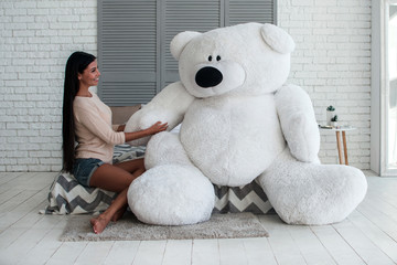 Nice to meet you! Beautiful young woman hugging huge teddy bear and keeping eyes closed with smile...