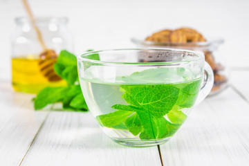 Mint tea in a cup, honey jar on a white wooden table.