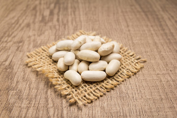 Navy Bean legume. Grains on square cutout of jute. Wooden table. Selective focus.