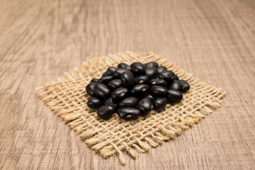 Black Turtle Bean legume. Grains on square cutout of jute. Wooden table. Selective focus.