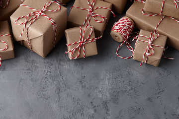 Christmas gift or present boxes wrapped in kraft paper with striped baker's twine string on textured stone background, copy space