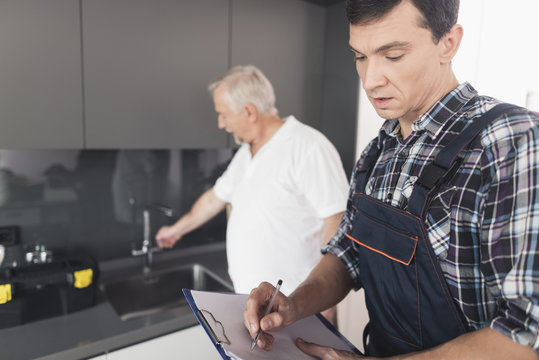 Two men of plumbers are standing in the kitchen. An elderly man inspects the place of repair work.