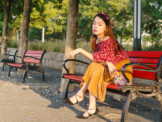 Portrait of a beautiful Chinese girl sitting in a bench in sunny autumn day.