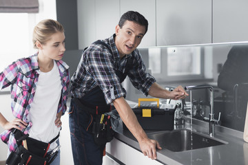 Obraz premium A man and a woman plumber repair a kitchen faucet from the client at home.