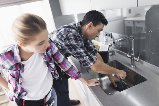 A man and a woman plumber repair a kitchen faucet from the client at home.
