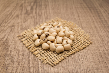 Black Eyed Pea legume. Grains on square cutout of jute. Wooden table. Selective focus.