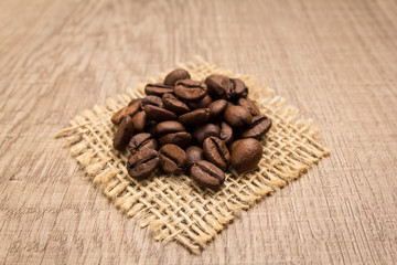coffee beans seed. Grains on square cutout of jute. Wooden table. Selective focus.