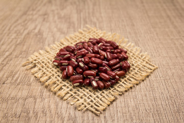 Adzuki Bean legume. Grains on square cutout of jute. Wooden table. Selective focus.