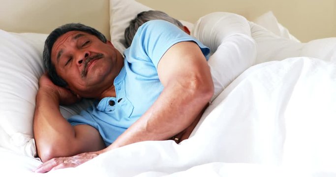 Senior man getting disturbed with woman snoring on bed 