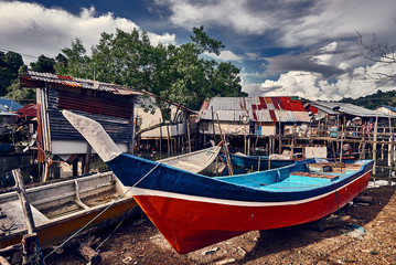 Fototapeta na wymiar Old colorful asian fishing boats and dramatic sky on the background. Traditional asian fishing village, Langkawi island, Malaysia.