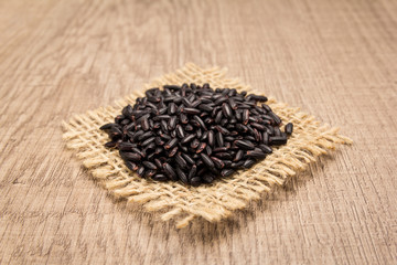 Black Rice seed. Grains on square cutout of jute. Wooden table. Selective focus.