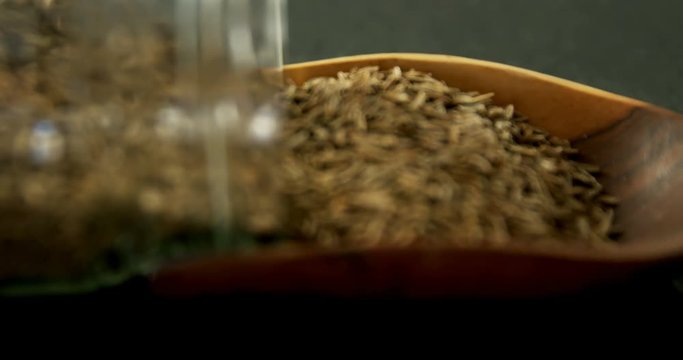 Cumin spilling out of jar into scoop 