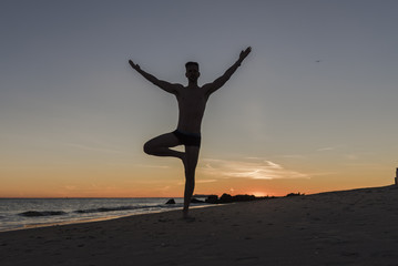 Fototapeta na wymiar Silhouetted man doing tree yoga pose at sunset on the beach