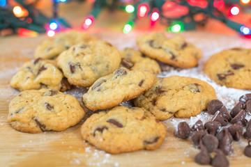 Freshly baked chocolate chip cookies on wooden board with colored lights in background, selective focus