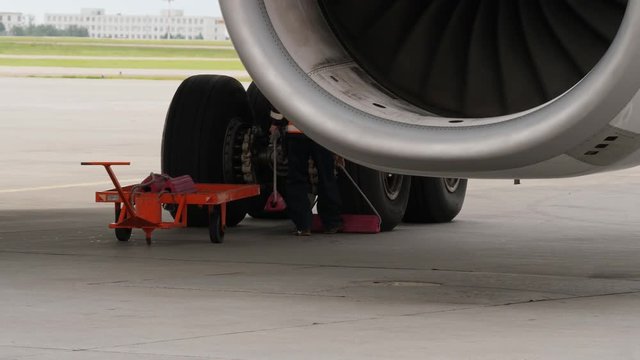 Ground crew member places chocks under aircraft wheels. View from behind jet engine
