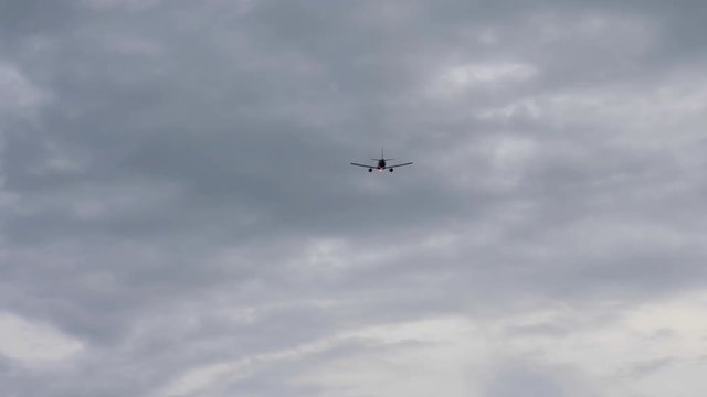Silhouette of jet airliner flying away in overcasted sky
