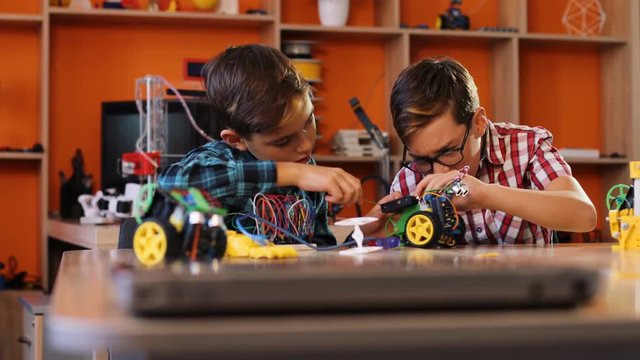 Close up of two boys using screwdrivers to assemble robotic machines on the table in the modern comfortable playing space. Boys giving five to each other in the end. Portrait