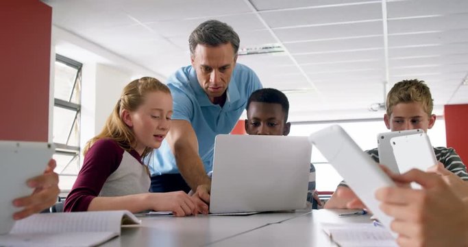 Teacher assisting schoolkids on laptop 