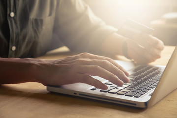 technology, shopping and banking concept - Close up of casual man holding credit card and using laptop on the table, toned with sunlight