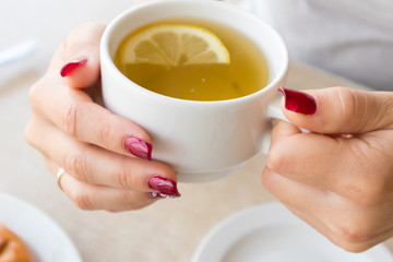 Woman's elegant red manicure and cup of green tea with lemon in cafe.