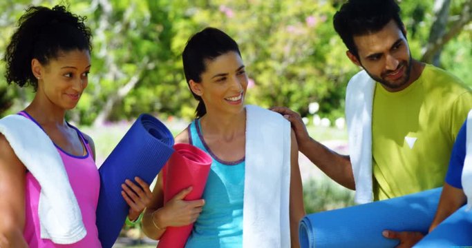 People with rolled exercise mats talking in the park 
