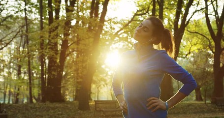 Young woman runner stretching her neck before jogging early in the morning in the beautiful green park. Outdoors