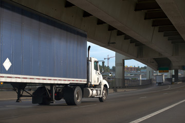 Big rig semi truck with day cab and covered tarp semi trailer going under overpass bridge