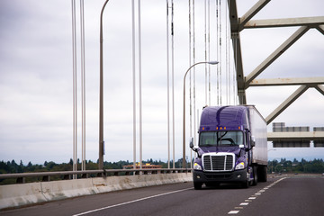 Purple big rig semi truck with dry van trailer for long haul cargo delivery running along arch bridge highway © vit
